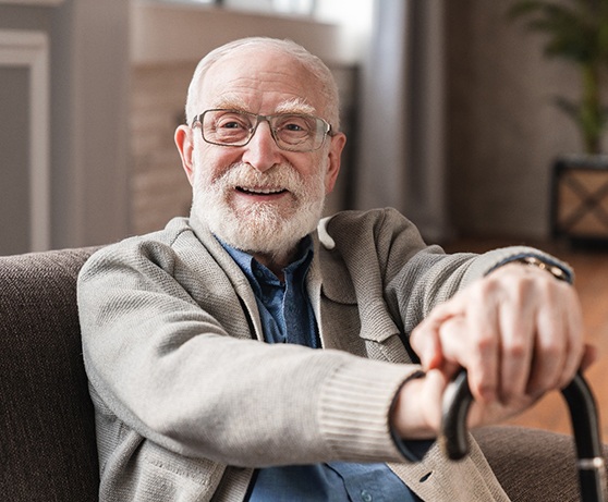 Senior man with glasses sitting on couch with cane