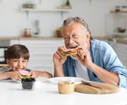 smiling man eating sandwiches with his grandchild
