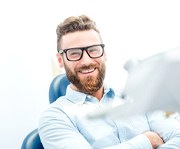Man in collared shirt and glasses smiling while sitting in a dental chair
