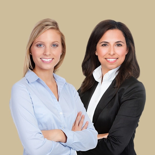 Two smiling women in business attire standing with their arms crossed