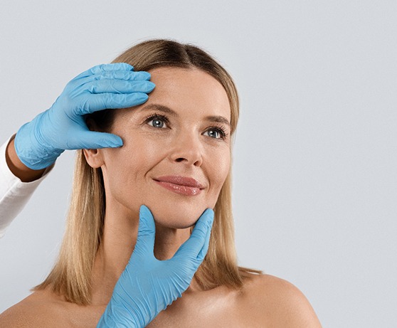 a smiling woman with gloved hands touching her face
