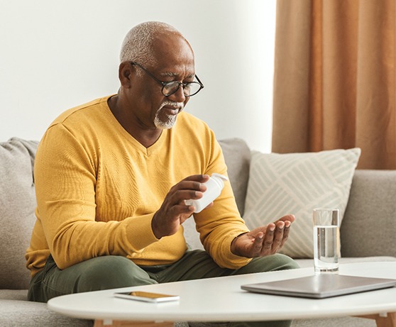a man sitting in his living room about to take a pill with water
