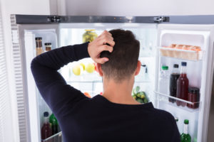 a person searching for a snack in their refrigerator while scratching their head